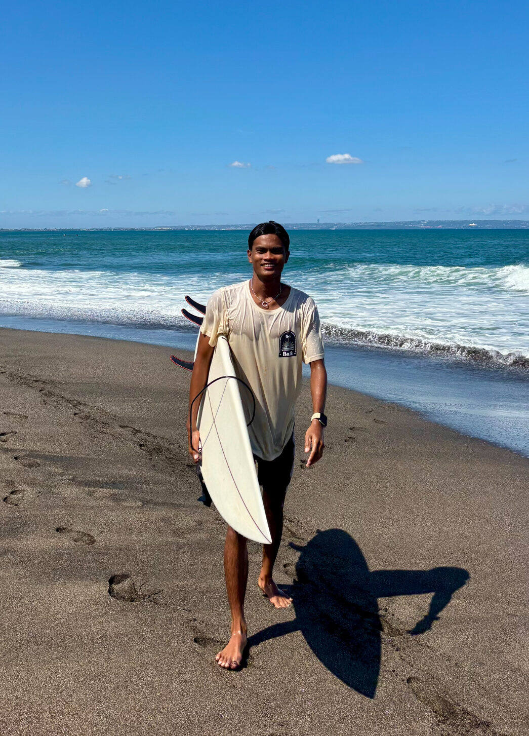 Surf coach Daffa with his surfboard on the black sand beach of Yeh Sumbul, Medewi