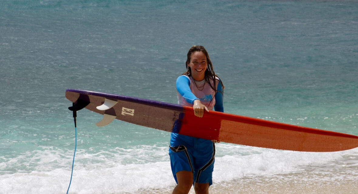 Surfer carrying her longboard out of the water at Medewi Beach, West Bali