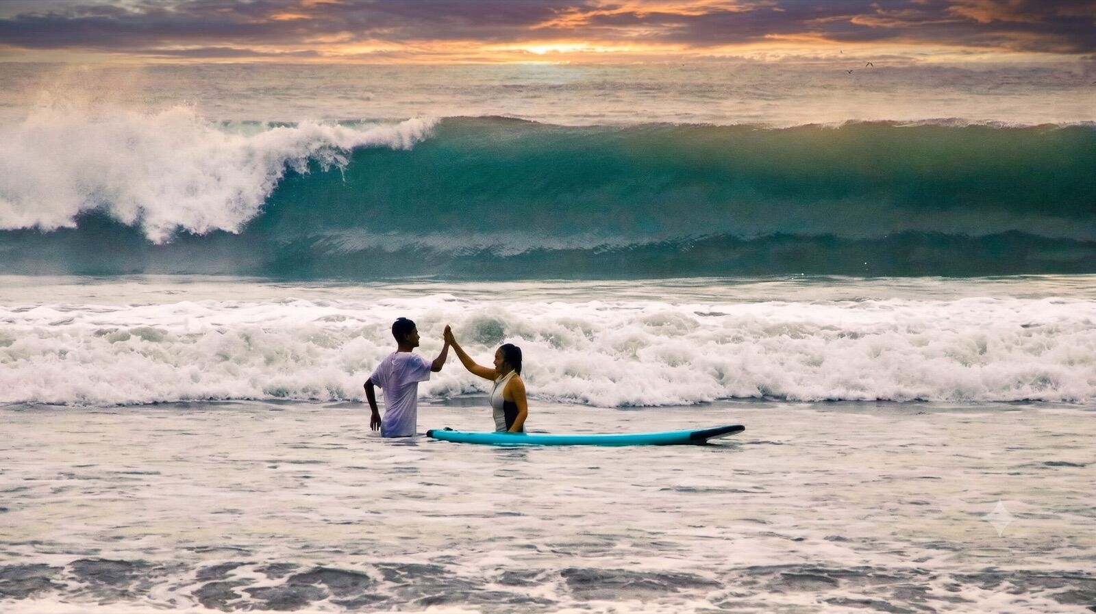 Surf coach and student sharing a high-five in front of a sunset wave in Medewi