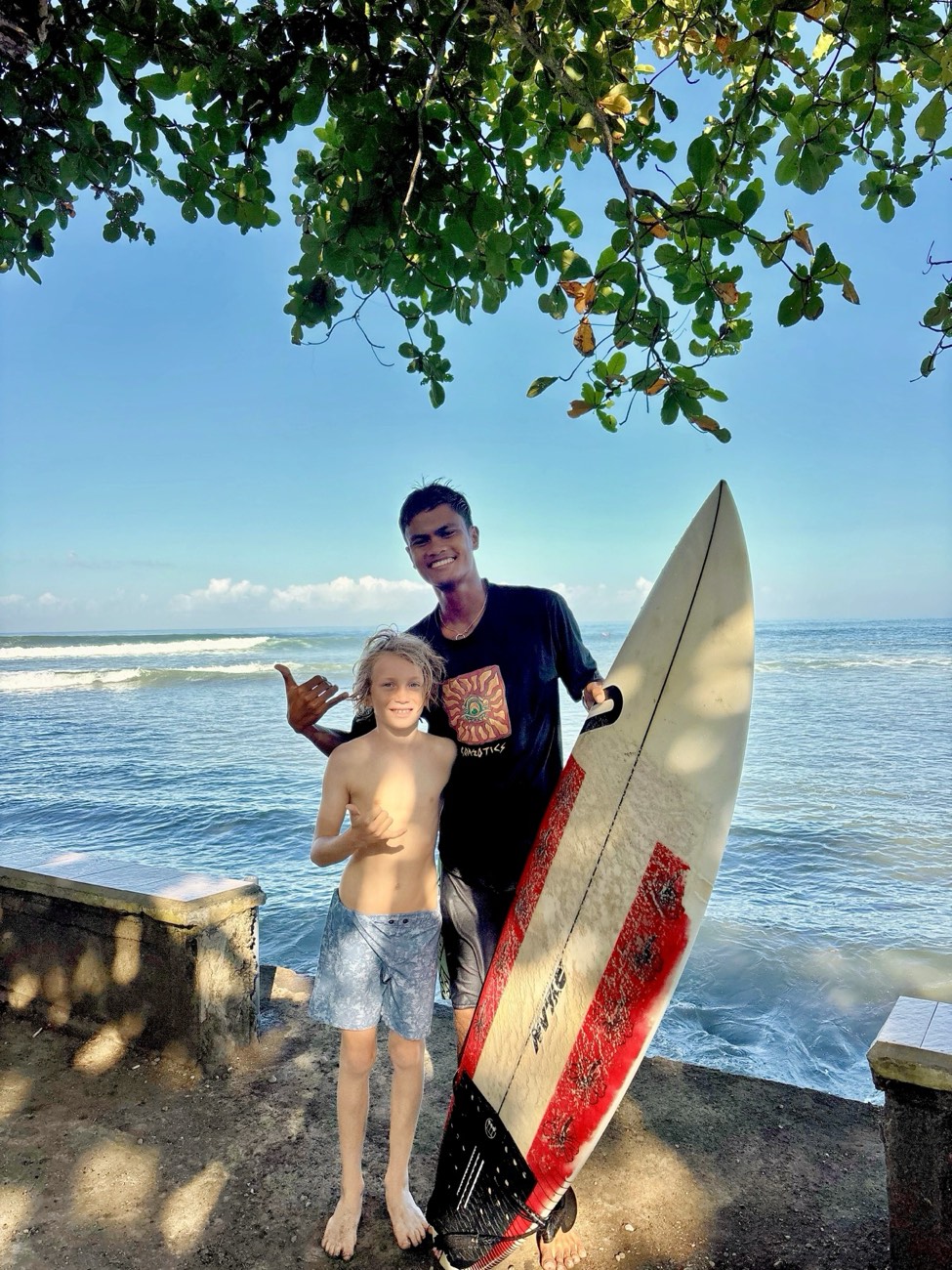 Coach Daffa with a young guest and a surfboard at the Medewi point