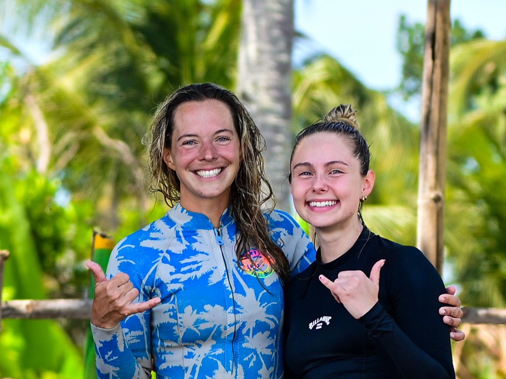 Two guests in wetsuits throwing shakas after coming out of the water