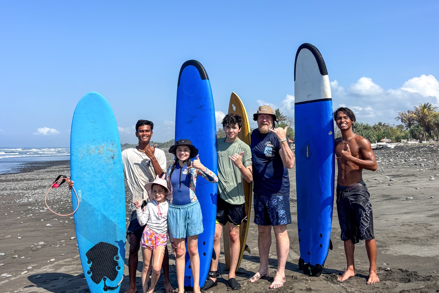 A family and their coaches with surfboards on the black sand at Medewi