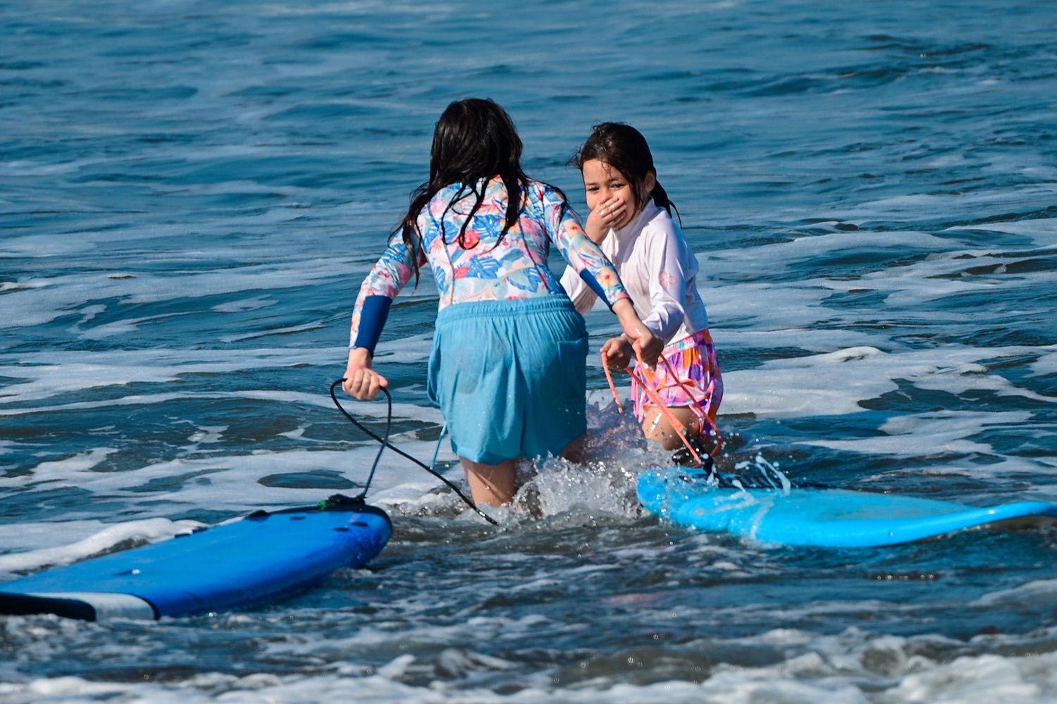 Two girls laughing in the shallows with their boards at Medewi